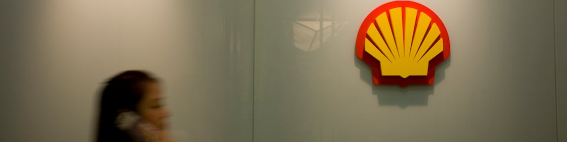 Mujer habla en teléfono móvil con la marca Shell al fondo