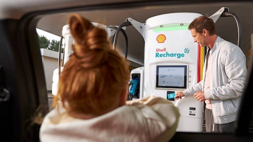 Un hombre usando una unidad de recarga Shell mientras una niña mira desde el interior de un automóvil