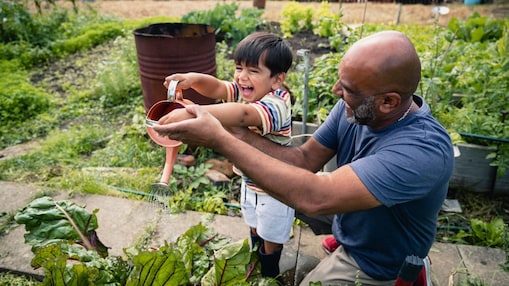 Hombre ayudando a un niño sonriente a regar plantas en un jardín