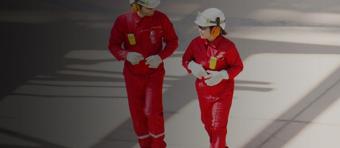 Trabajador y trabajadora con overoles rojos, cascos blancos y protección auditiva caminando