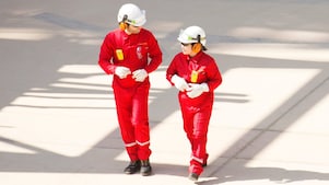 Trabajador y trabajadora con overoles rojos, cascos blancos y protección auditiva caminando